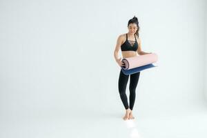 vol lengte portret van een jong vrouw Holding yoga mat geïsoleerd Aan wit achtergrond foto