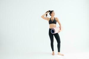 vol lengte portret van een jong vrouw Holding yoga mat geïsoleerd Aan wit achtergrond foto