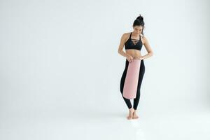 vol lengte portret van een jong vrouw Holding yoga mat geïsoleerd Aan wit achtergrond foto