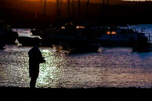 een Mens staand Aan de kust met een visvangst hengel foto