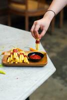 bijgesneden hand- dompelen aardappel plak naar saus dichtbij omhoog foto