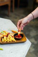 bijgesneden hand- dompelen aardappel plak naar saus dichtbij omhoog foto