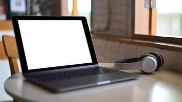 mockup laptop leeg scherm en hoofdtelefoon op geplaatst op een tafel in een café. foto