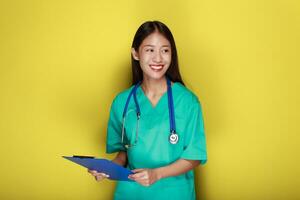 portret van een mooi jong vrouw in een geel achtergrond, Aziatisch vrouw vervelend een dokter uniform maakt een glimlachen uitdrukking, een jong vrouw vervelend een medisch stethoscoop heeft een vriendelijk uitdrukking. foto