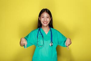 portret van een mooi jong vrouw in een geel achtergrond, vriendelijk mooi vrouw vervelend een dokter uniform en richten terwijl vervelend een stethoscoop. foto