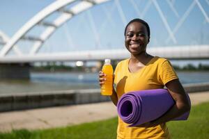 sportief vrouw drinken energie drinken en Holding oefening mat foto