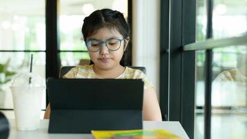 Aziatisch meisje met een bril die naar tablet kijkt om online te studeren. foto