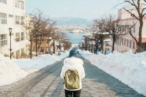 vrouw toerist bezoekende in hakodate, reiziger in trui bezienswaardigheden bekijken hachiman zaka helling met sneeuw in winter. mijlpaal en populair voor attracties in hokkaido, Japan. reizen en vakantie concept foto