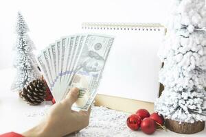 teder handen wieg geld met een wit scherm mock-up en wit kalender met een feestelijk tafereel van een mooi Kerstmis boom versierd, met Kerstmis ballen, pijnboom kegels, en een rood huis geschenk doos. foto