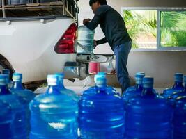 arbeiders optillen drinken water Doorzichtig en schoon in blauw plastic gallon in de terug van een vervoer vrachtauto gezuiverd drinken water binnen de productie lijn klein bedrijf foto