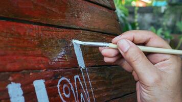 detailopname van handen van jong vrouw schilder creëren kunst gebruik een penseel naar trek wit belettering ontwerpen Aan een houten koffie winkel teken.buiten activiteiten, mensen aan het doen activiteiten. foto