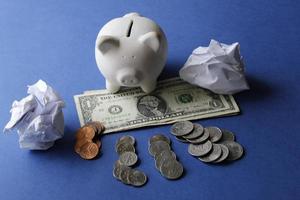 Amerikaanse bankbiljetten, munten, wit spaarvarken en verfrommelde papieren ballen op de blauwe achtergrond foto