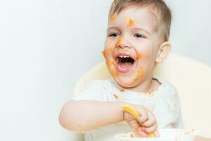 schattig baby jongen terwijl aan het eten besmeurd zijn gezicht met een pompoen foto