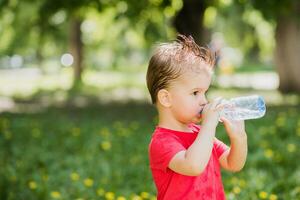 knap jongen drankjes Doorzichtig water van een fles Aan een zonnig dag buiten foto