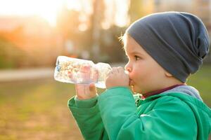 knap jongen drankjes Doorzichtig water van een fles Aan een zonnig dag buiten foto