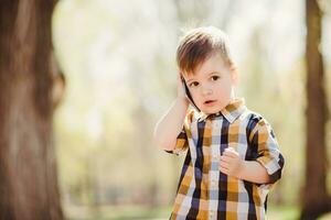 schattig jongen spreekt door mobiel telefoon in de park foto