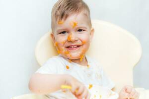 schattig baby jongen terwijl aan het eten besmeurd zijn gezicht met een pompoen foto