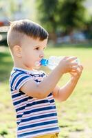 knap jongen drankjes Doorzichtig water van een fles Aan een zonnig dag buiten foto