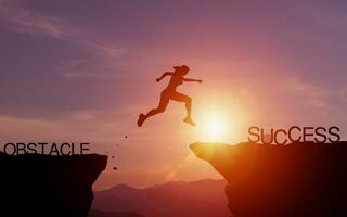 inspanning en inzet naar succes. silhouet van vrouw jumping over- een klif naar bereiken succes met avond zonlicht. concept van instelling doelen voor succes en effectief oplossen problemen en obstakels foto