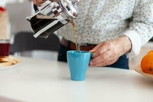 ouder Mens morsen koffie in kop na maken het gebruik makend van Frans druk op voor ontbijt in keuken. ouderen persoon in de ochtend- genieten van vers bruin cafe espresso kop cafeïne van wijnoogst mok. foto