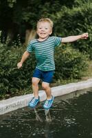 weinig jongen jumping in een plas in zomer foto