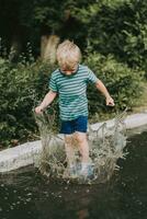 weinig jongen jumping in een plas in zomer foto