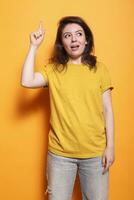 positief vrouw staand over- geïsoleerd oranje achtergrond met inhoudsopgave vinger richten omhoog. in studio, Kaukasisch vrouw volwassen hebben een Super goed idee terwijl gebaren en op zoek omhoog. foto