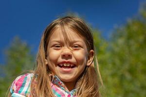 portret van Kaukasisch weinig meisje van 6 7 jaren glimlachen en op zoek Bij camera over- blauw lucht foto