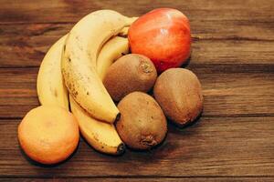 fruit banaan, kiwi, appel, mandarijnen liggen Aan een houten tafel. foto