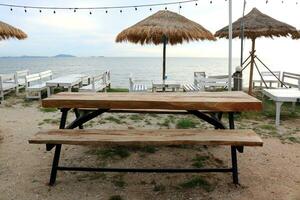 bruin hout tafel en bank Aan zand met zee en helder lucht achtergrond, Thailand. foto