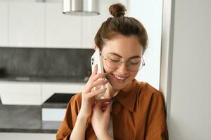 portret van lief jong vrouw antwoorden telefoon telefoontje en lachend, leunend Aan muur, staand Bij huis en pratend Aan telefoon foto