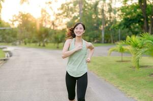 fit Aziatisch jong vrouw jogging in park glimlachen gelukkig rennen en genieten van een gezond buitenshuis levensstijl. vrouw jogger. geschiktheid loper meisje in openbaar park. gezond levensstijl en welzijn wezen concept foto