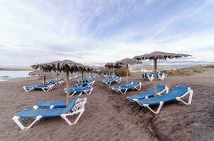 een strand met lounge stoelen en paraplu's Aan het foto