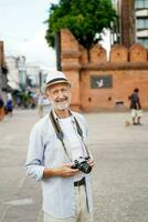 detailopname Amerikaans senior toerist Mens acteren voor fotograaf Aan gebraamd de Chiang mai stad poort mijlpaal achtergrond. senior toerist concept foto