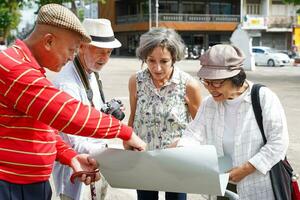 groep van senior toerist zijn op zoek Bij stad kaarten naar vind toerist attracties Aan wazig van stad achtergrond. foto