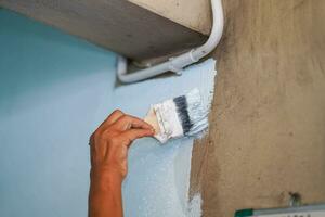 detailopname hand- van de schilder Holding een verf borstel schilderij wit kleuren Aan de muur van huis. foto