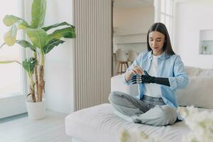 sereen vrouw met een bionisch arm comfortabel zit Bij huis, presentatie van harmonie tussen technologie en dagelijks leven foto