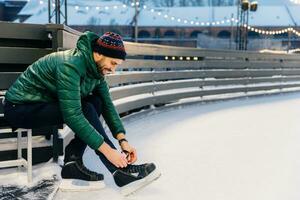 gefocust Mens vetersluiting omhoog ijs skates Bij een besneeuwd baan, met warm lichten in achtergrond foto