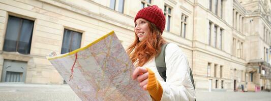 roodharige meisje, toerist onderzoekt stad, looks Bij papier kaart naar vind manier voor historisch oriëntatiepunten, vrouw Aan haar reis in de omgeving van Europa zoekopdrachten voor bezienswaardigheden bekijken foto