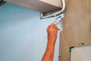 detailopname hand- van de schilder Holding een verf borstel schilderij wit kleuren Aan de muur van huis. foto