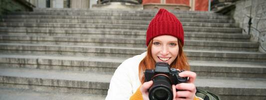 jong leerling, fotograaf zit Aan straat trap en cheques haar schoten Aan professioneel camera, nemen foto's buitenshuis foto