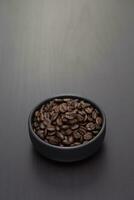 donker geroosterd koffie bonen in een klein zwart keramisch schaal. foto