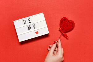 lichtbak met opschrift worden mijn valentijn. vrouw hand- houdt een opengewerkt Valentijn hart Aan stok. Valentijnsdag dag groet kaart foto