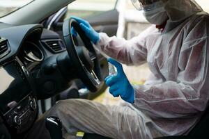 ontsmettingsmiddel arbeider karakter in beschermend masker en pak sprays bacterieel of virus in een auto. foto