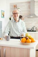 ouderen Mens in keuken glimlachen op zoek Bij camera Holding heet koffie beker. portret van ontspannen ouder persoon in de ochtend, genieten van vers warm drankje. gezond glimlachen volwassen gezicht foto