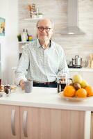 senior Mens in keuken glimlachen op zoek Bij camera Holding heet koffie beker. portret van ontspannen ouderen ouder persoon in de ochtend, genieten van vers warm drankje. gezond glimlachen volwassen gezicht foto