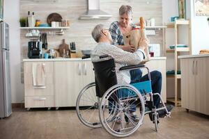 senior vrouw nemen kruidenier papier zak van gehandicapten man in rolstoel. volwassen mensen met vers groenten van markt. leven met gehandicapt persoon met wandelen handicaps foto