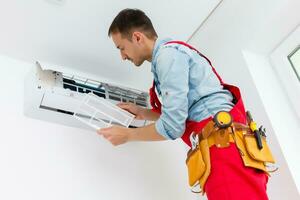 jong Mens repareren lucht conditioner staand Aan trapladder foto