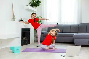 twee weinig meisjes beoefenen yoga, uitrekken, geschiktheid door video Aan notebook. ver weg online onderwijs opleiding, aëroob Bij huis. gezond levensstijl, coronavirus, blijven huis. kinderen sport huis quarantaine. foto