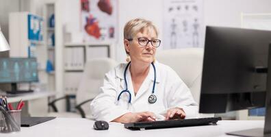 volwassen vrouw dokter gebruik makend van computer in ziekenhuis kastje. foto